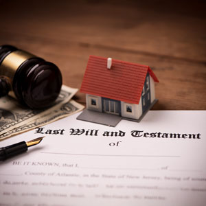 Last Will and Testament document with a gavel, miniature house, and dollar bills on a wooden desk